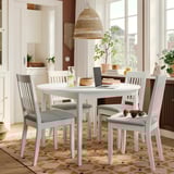 NÄSINGE white round dining table with 4 chairs, grey cushioned seats, solid wood legs, placed on a patterned rug near a window.