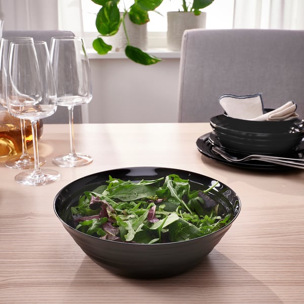 Black bowl with salad on wooden table, wine glasses, plates, and napkins.