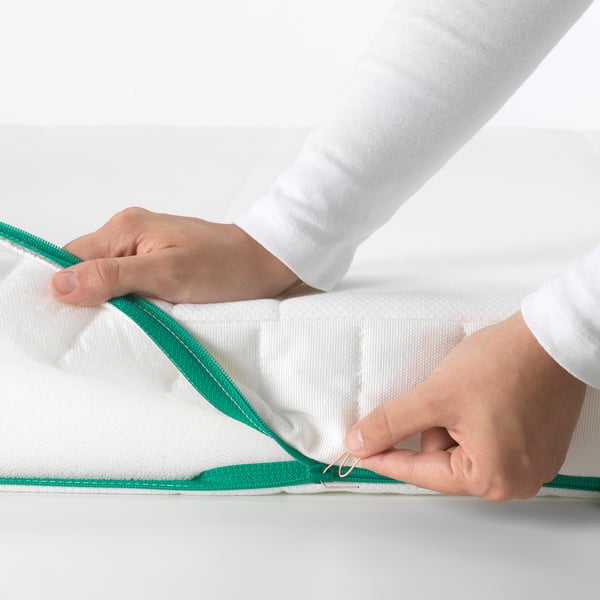A person is shown securing a green zipper on a white mattress, highlighting its child-safe feature with a small loop.