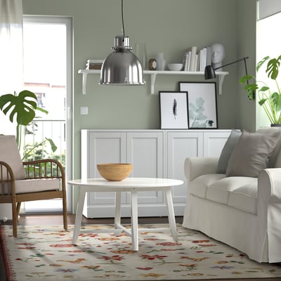 Living room with green walls, white furnishings, and NICKGRÄS rug. Coffee table and window enhance the cheerful atmosphere.