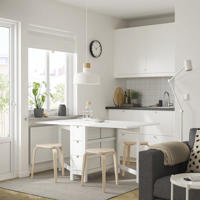 White kitchen with NORDEN table, stools, sleek counter, black accents, and large window.