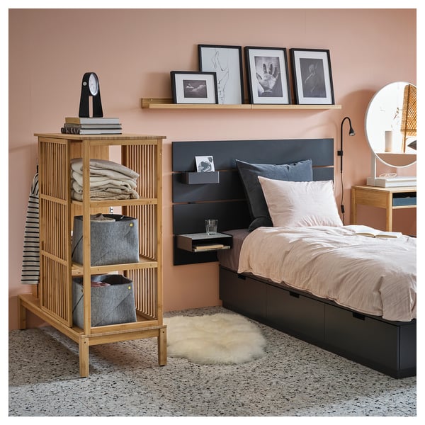 Modern bedroom with pink walls, featuring a wooden storage unit, bed with gray pillows, and framed photos.