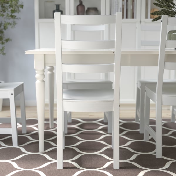 Three ladder-back wooden chairs around light table on rug.