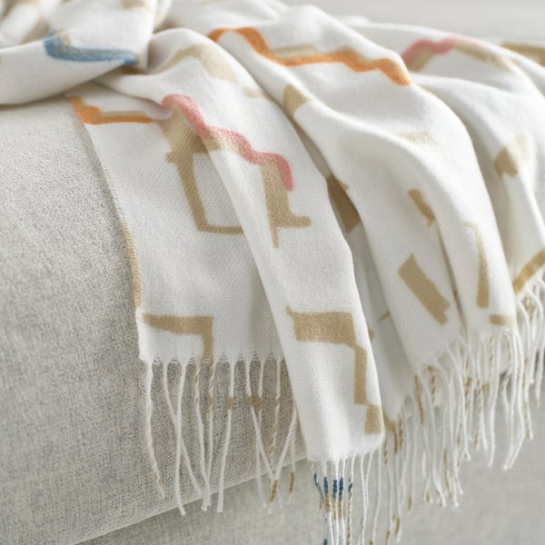 Folded white throw blanket with orange, green, and blue patterns, fringed edges; high-quality, soft appearance.