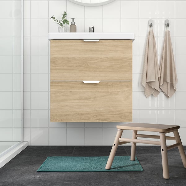 Modern bathroom with wooden vanity, white tiles, green OSBYSJÖN mat, and contrasting stool.