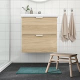 Modern bathroom with wooden vanity, white tiles, green OSBYSJÖN mat, and contrasting stool.