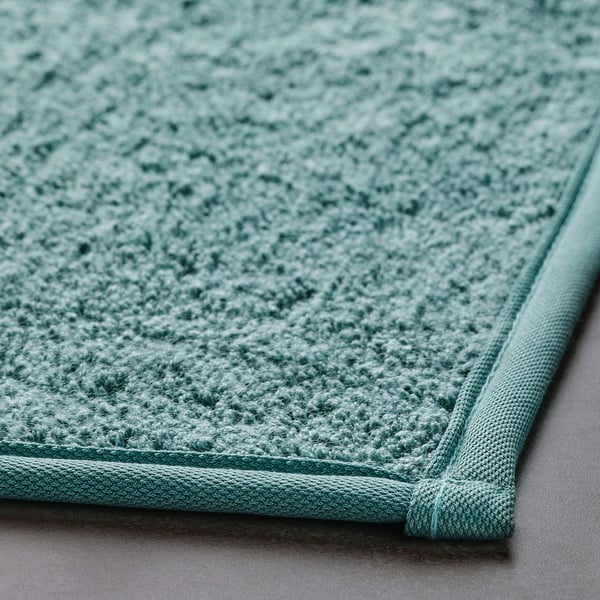 Soft, light green bath mat with textured surface and bordered edge providing comfort and non-slip grip.