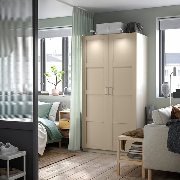 Modern bedroom featuring beige PAX wardrobe with integrated lighting, light wood flooring, blue-green curtains, and cozy decor.