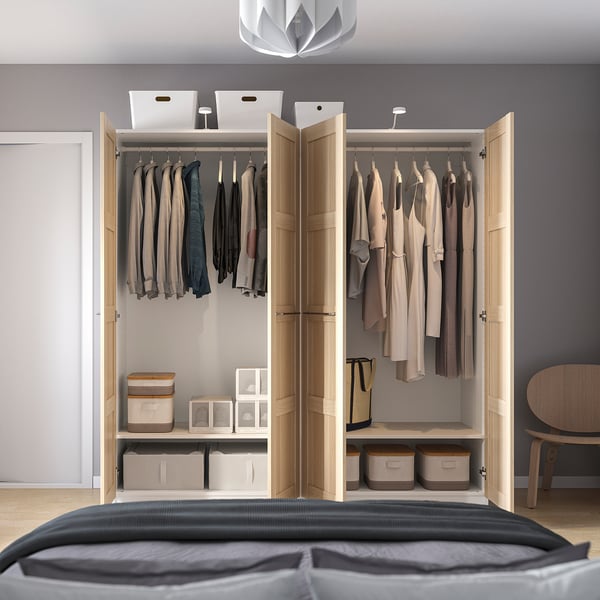 Open wooden closet revealing clothes hangers, storage bins, and shelves with boxes, standing next to a bed.