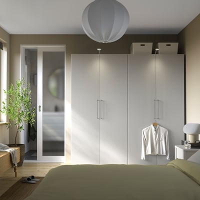 Modern bedroom with large white PAX wardrobe, sleek handles, and green bed. Hanging white shirt, pendant light, and wooden floor.