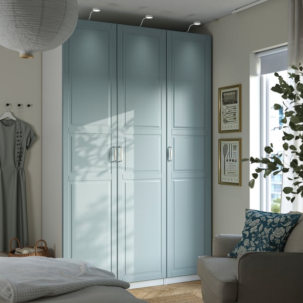 Bedroom with large blue PAX wardrobe, floral sofa, pendant lamp, and natural light.