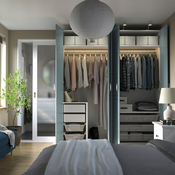 Modern bedroom with open PAX wardrobe, lamp, and plant.