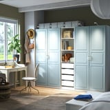 Light blue PAX wardrobe with shelves & drawers, against green wall, above white chair.