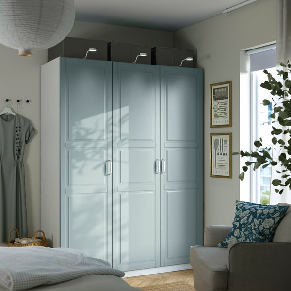 Modern blue bedroom with PAX wardrobe, mirrored door, black boxes, gray chair, plant, dress, cozy space.