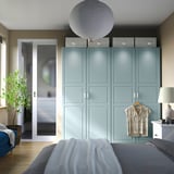 Modern bedroom with large light blue PAX wardrobe, wooden floor, and hanging garment. Soft lighting, gray bed, and glass door.
