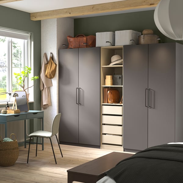 Grey PAX wardrobes by green wall, sleek handles, white shelving. Small desk, chair, plant, window light. Wooden floors, exposed beams.