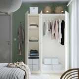 A green bedroom a white open wardrobe with shelves, a clothes rail holding shirts and boxes, and a grey robe on the wall.