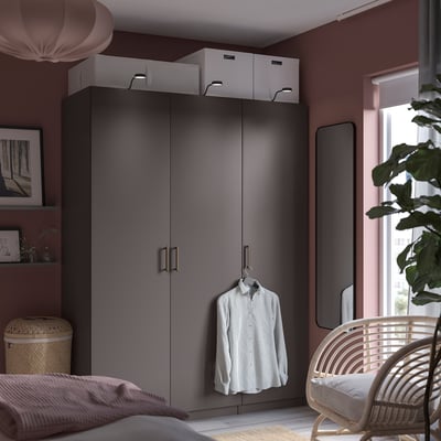 A modern bedroom a gray PAX wardrobe with hanging shirt, pink walls, and a wicker chair.