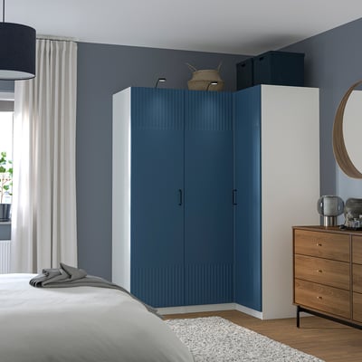 Modern blue PAX wardrobe fits corner, tall with white sides, next to wooden dresser and large mirror.