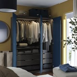 Bedroom with open blue PAX wardrobe, showing clothes, drawers, and shelves with lighting.