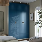 A tall blue PAX wardrobe with gold handles and mirror, next to a bed and window.