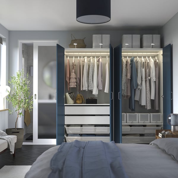 Modern bedroom with open PAX wardrobe displaying hangers, drawers, and neatly folded clothes.