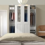 Sleek white PAX wardrobe with glass panels, displaying colorful clothes, storage boxes, and a wicker chair.