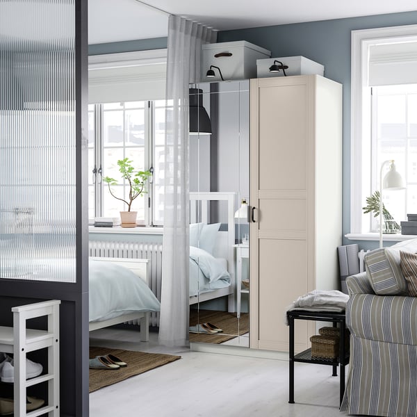 A living space featuring a PAX wardrobe, mirrored cabinet, bed with white linens, striped sofa, plant, and lamp.