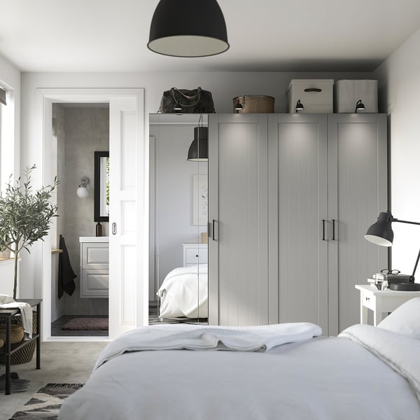 Modern bedroom with grey PAX wardrobe, glass doors, soft-close hinges, and desk with lamp. Bathroom sink visible.