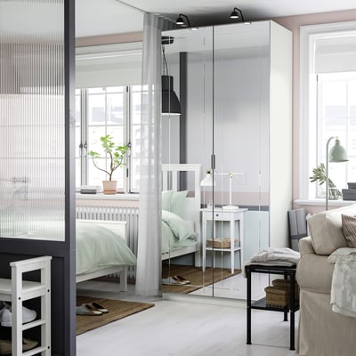 Modern bedroom with white PAX wardrobe featuring mirrored doors, reflecting light.