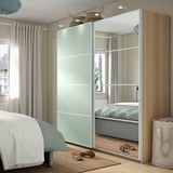 A bedroom featuring a tall, wide PAX wardrobe with light green and mirrored glass doors next to a bed.