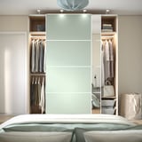 Modern bedroom with PAX wardrobe featuring sliding doors, hanging clothes, shelves with folded items, and integrated lighting.