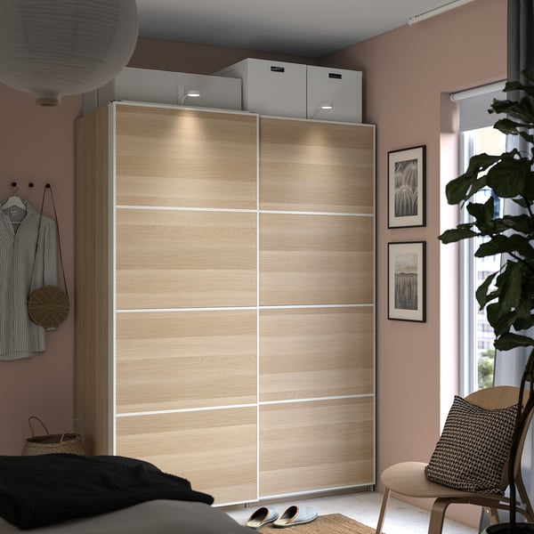 Modern bedroom with a large light wooden sliding door wardrobe, featuring integrated lighting, a cozy bed, and lush green plants.