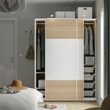 Modern wardrobe with sliding doors, hanging clothes, shelves, and storage baskets in a bedroom setting.