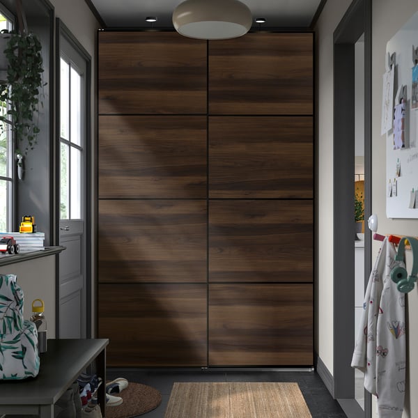 Large wooden PAX wardrobe centres room, surrounded by smaller furniture, with modern dark tones and minimalist design.