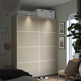 Bedroom with beige PAX wardrobe, sliding doors, white boxes, striped shirt, plant, and wooden chair.