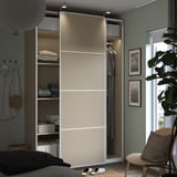 Modern bedroom with sleek beige PAX wardrobe, sliding doors, folded clothes, and plants.