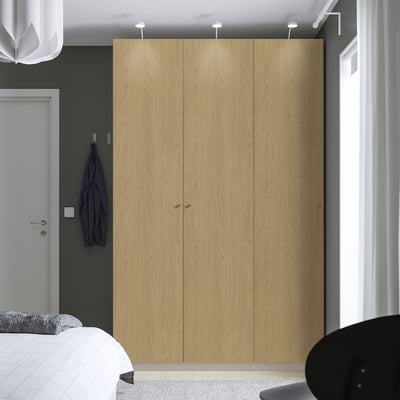Large wooden wardrobe stood between door and window. Simple design with minimalist handles. Hangs a blue jacket on its left side.