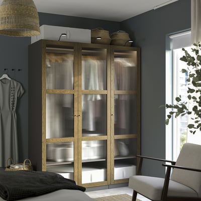 Modern bedroom with light wood PAX wardrobe and glass doors beside a window.
