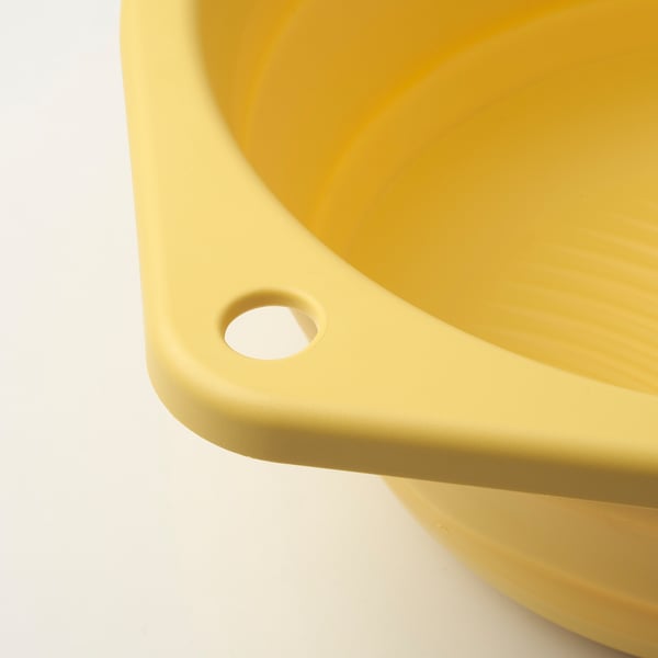 Bright yellow plastic washbasin collapsed into a flat disc, showing sturdy and space-saving design.