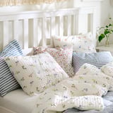 Bed with floral quilt and striped pillows in soft light. Pillowcases have envelope closure.