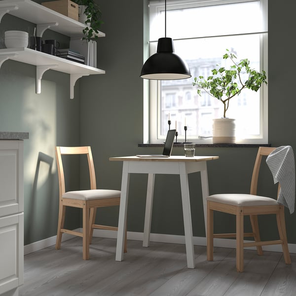 Small, modern kitchen with white table & wooden chairs. Hanging lamp and greenery add style. Table seats 2, fits well under open shelves.