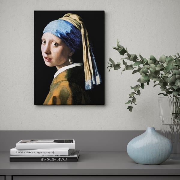 Picture of girl with a pearl earring on canvas hangs on wall over shelf with books and vases.