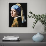 Picture of girl with a pearl earring on canvas hangs on wall over shelf with books and vases.
