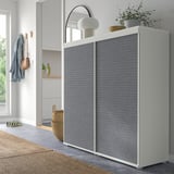 Modern closet with grey sliding doors, white frame. Decorated with plants, lamp, and mirror. Large, stands near a window.