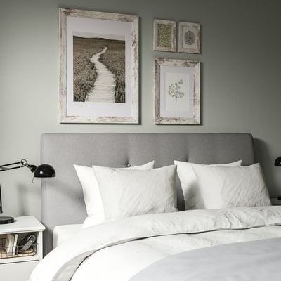 Cozy bedroom with gray headboard, rustic landscape print, black lamp, and white nightstand.