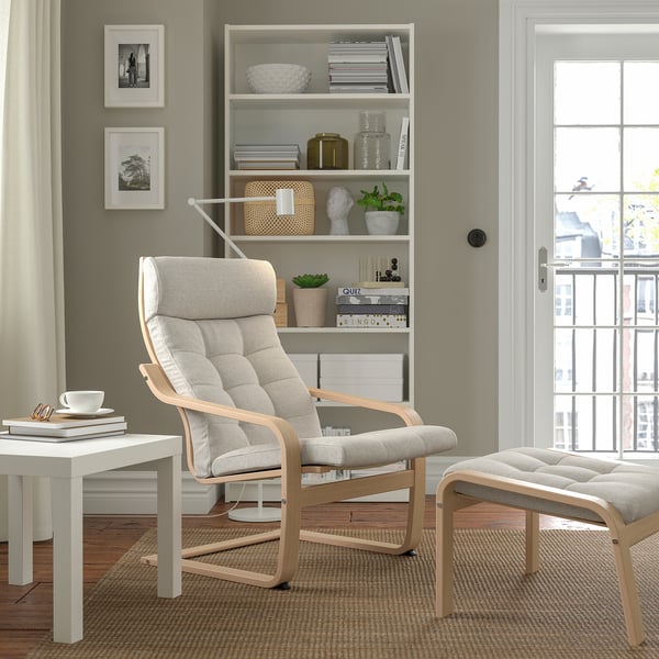 Modern living room with light grey POÄNG armchair & footstool, wooden frame, comfy cushions, next to white side table & bookshelf.