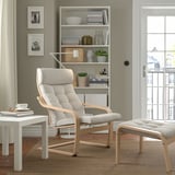 Modern living room with light grey POÄNG armchair & footstool, wooden frame, comfy cushions, next to white side table & bookshelf.