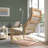 Modern living room with a brown POÄNG armchair featuring a high back for neck support, positioned near a window on a multicolored rug.