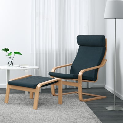 Modern living room with POÄNG chair, footstool, & decor. Dark blue cushions, oak arms.